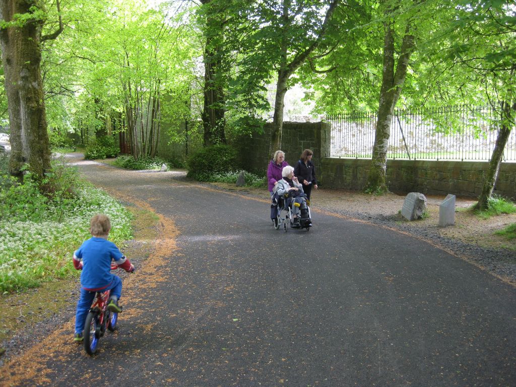 A child on a bicycle races down the path at Coole Park as Annis Householder and Martha Clark stroll with Roberta Clark, looking for deer in the enclosure to their left.