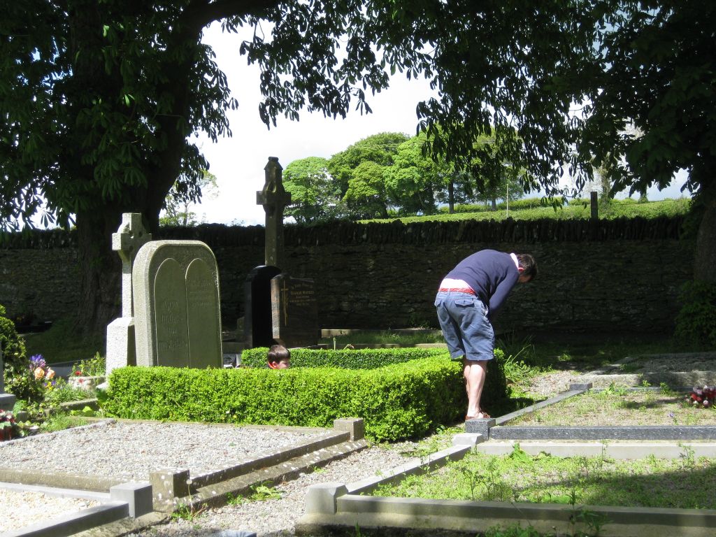 It was Trinity Sunday, a traditional day for grooming gravesites. Here, a father trims the hedge at a gravesite while his young son (playing on the grave) keeps him company and chats.